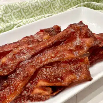 bacon cooked in the oven on a white platter with a green print napkin