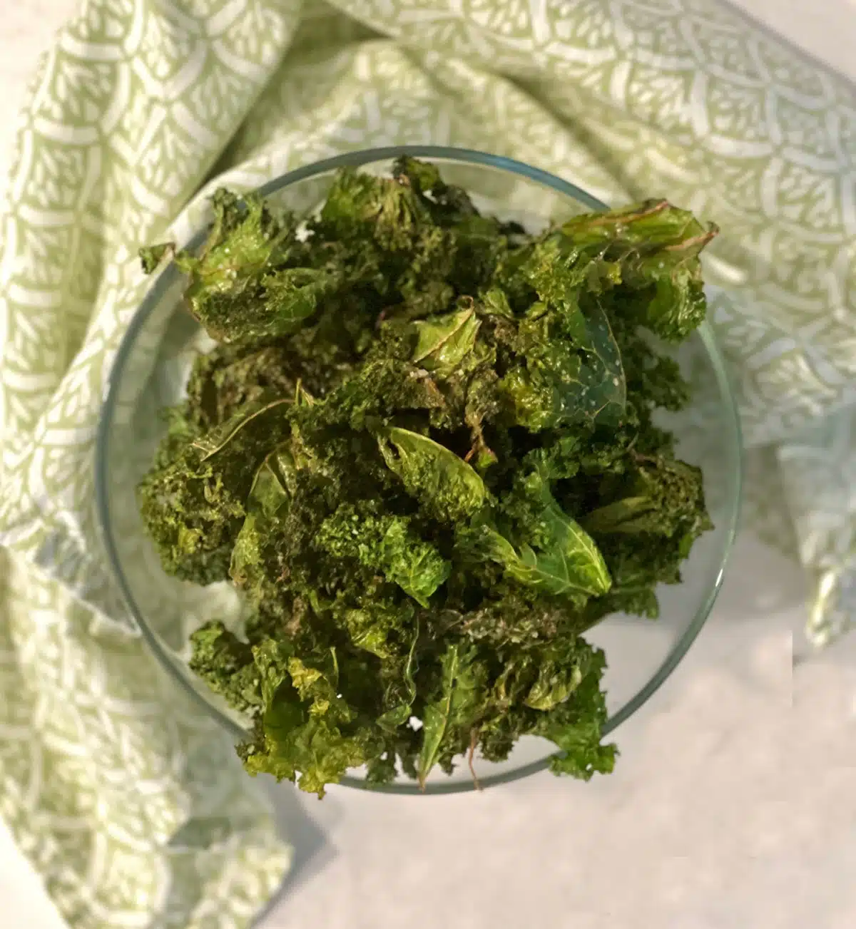 overhead photo of a bowl of air fried kale chips with green napkin