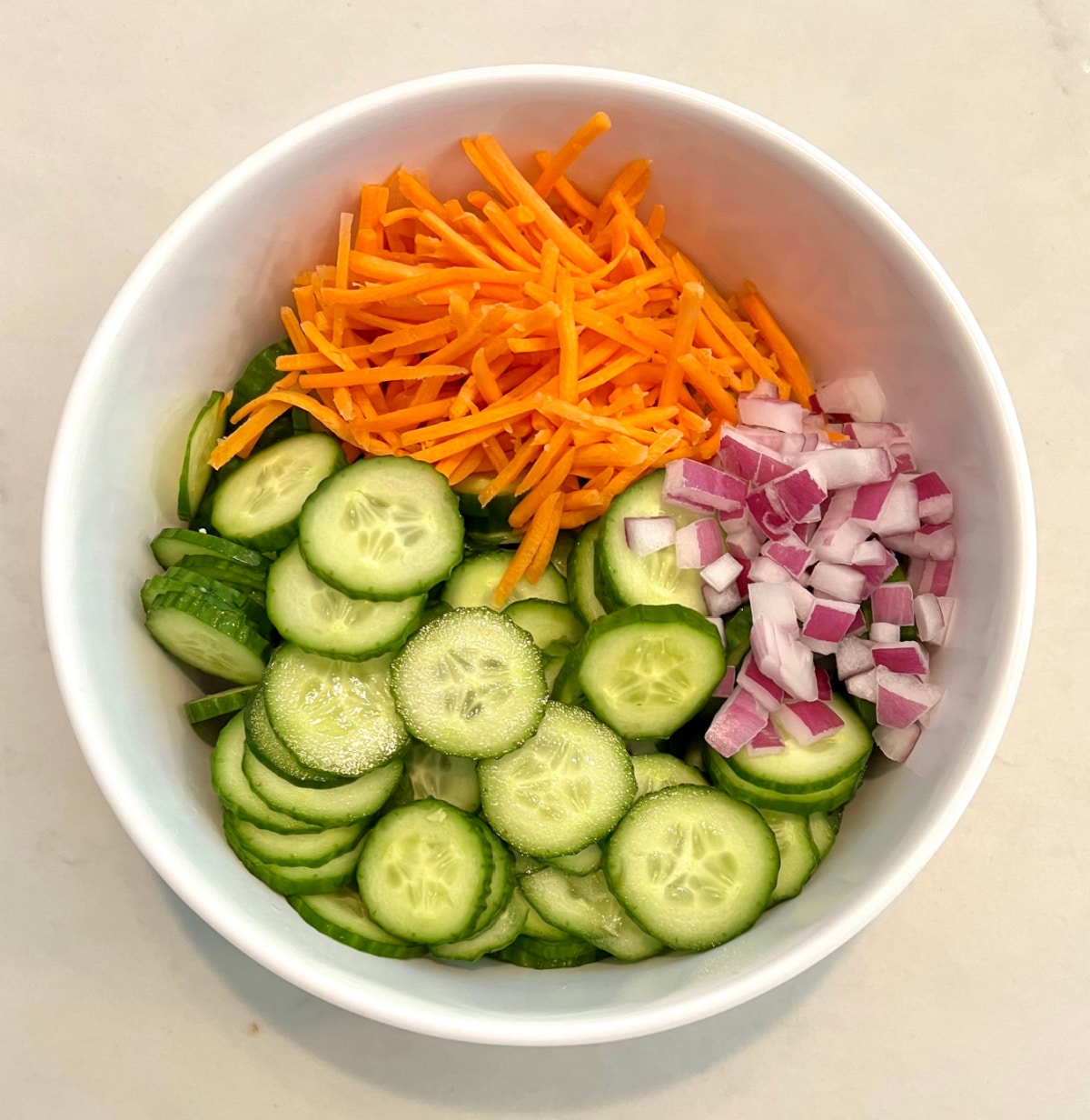 cucumber, carrot ans red onion in a mixing bowl