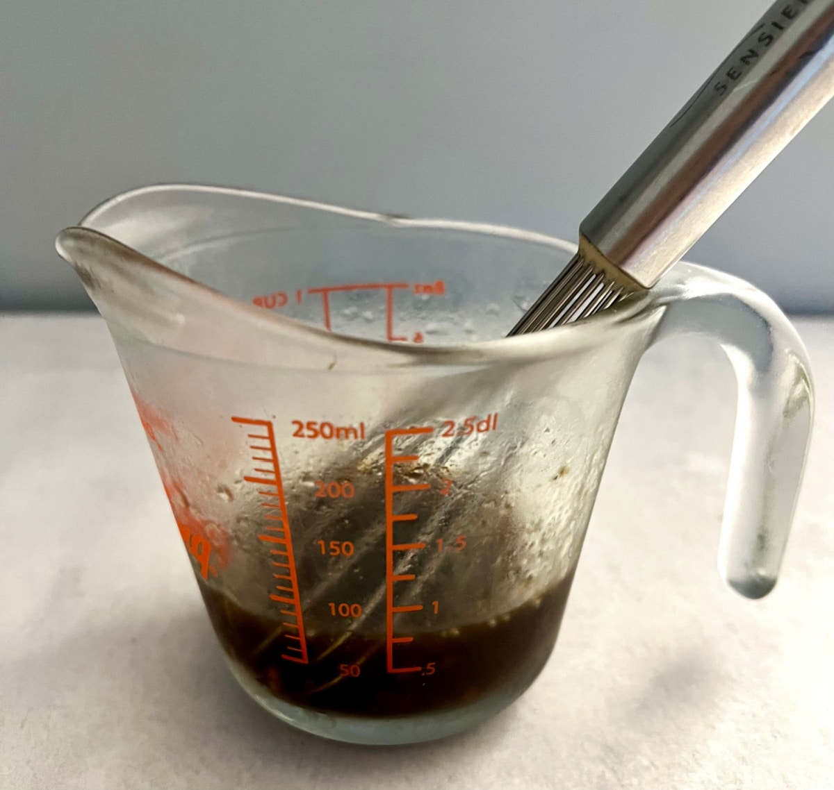 measuring cup with salad dressing and whisk