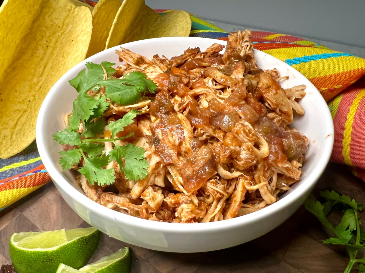 shredded chicken taco meat in a bowl with fresh cilantro sprigs