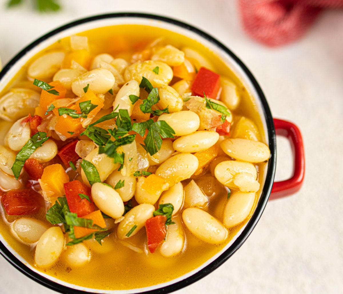 overhead of butter bean stew in red bowl with handles