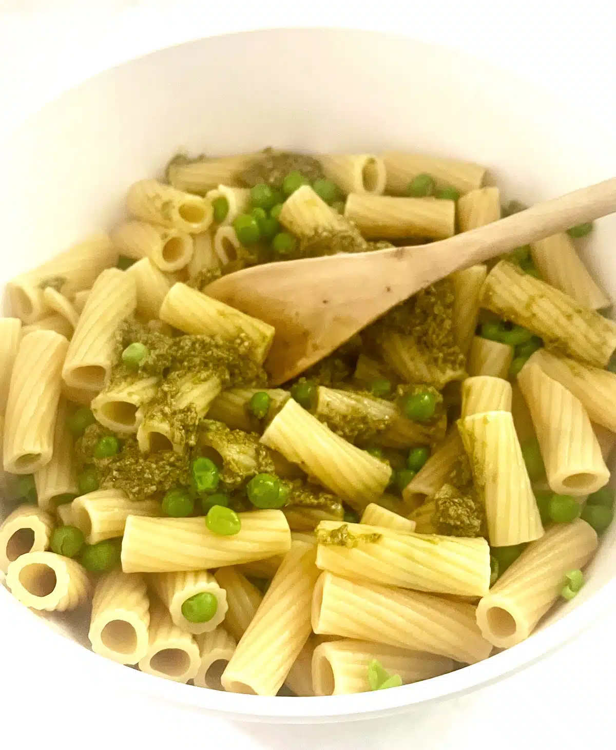 tossing pasta, peas and pesto together in a bowl