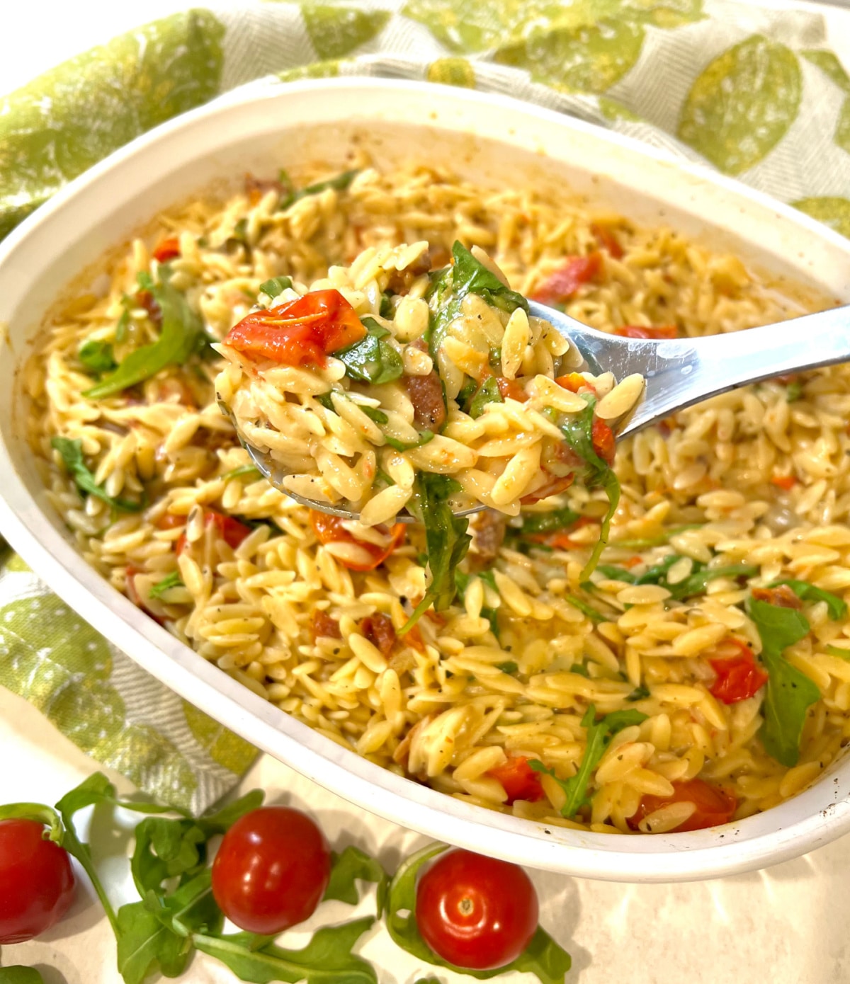 serving spoon with baked orzo over the baking dish