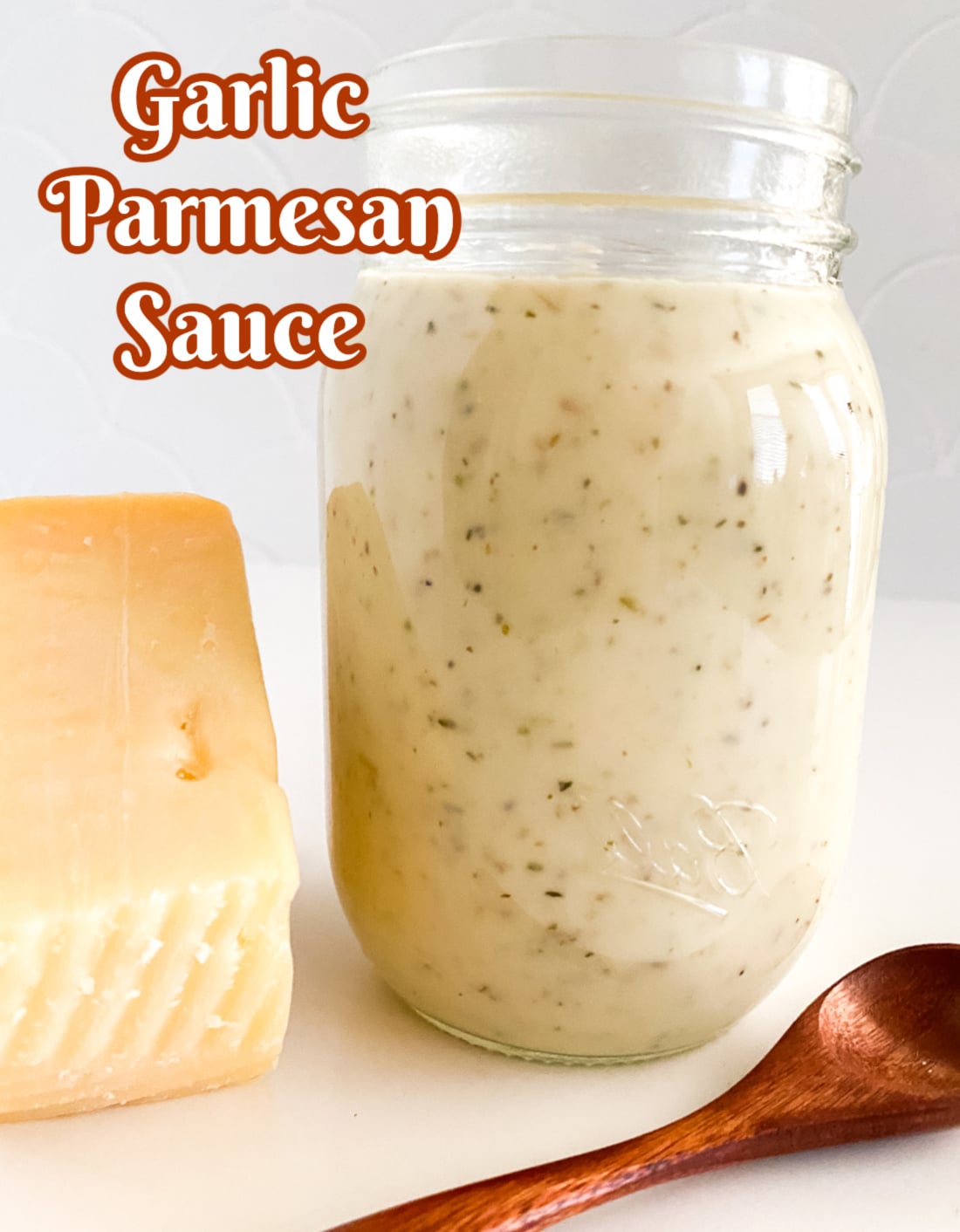 Garlic Parmesan Sauce in a jar with a wedge of cheese and a wooden spoon
