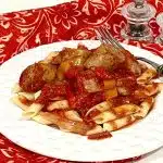 slow cooker sausage and peppers over pasta on a white plate