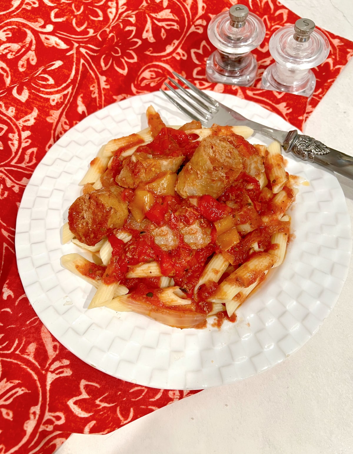 overhead of crockpot sausage and peppers over pasta with a fork on a white plate