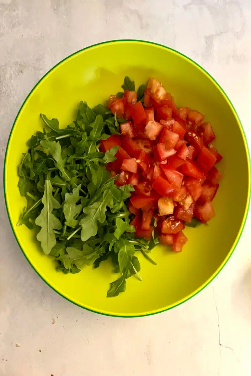 combining baby arugula and chopped tomatoes n a bowl