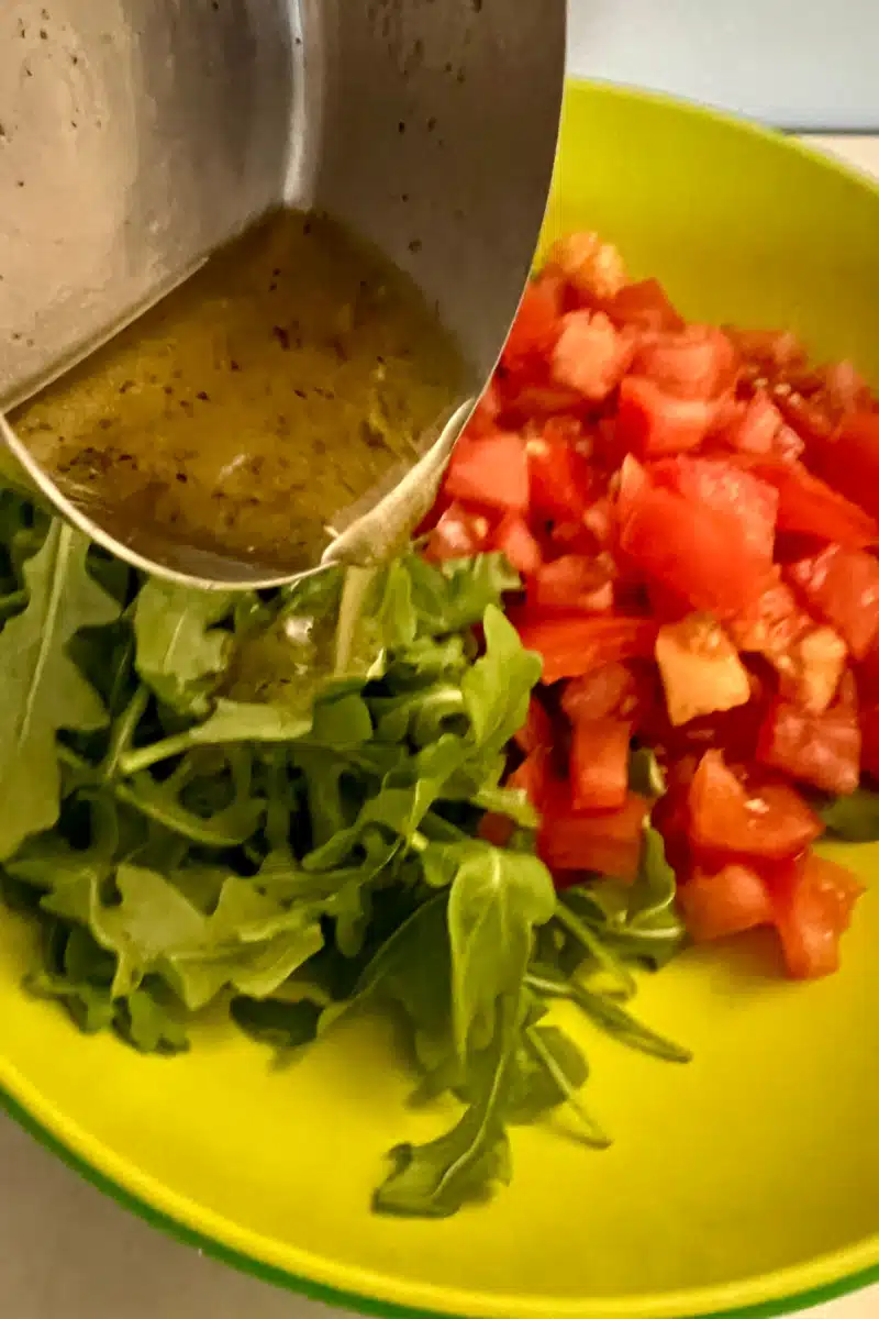 adding vinaigrette to the baby arugula and tomatoes