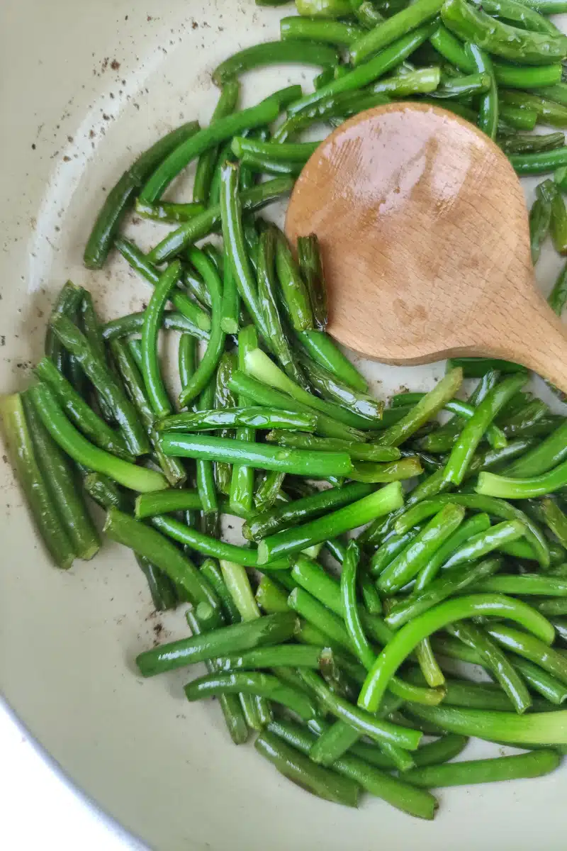 cooking garlic scapes in a skillet with wooden spoon