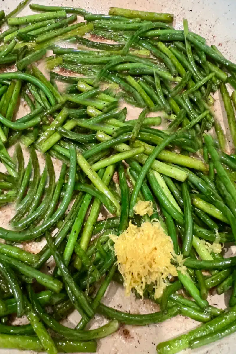 adding lemon zest to garlic shoots in a skillet
