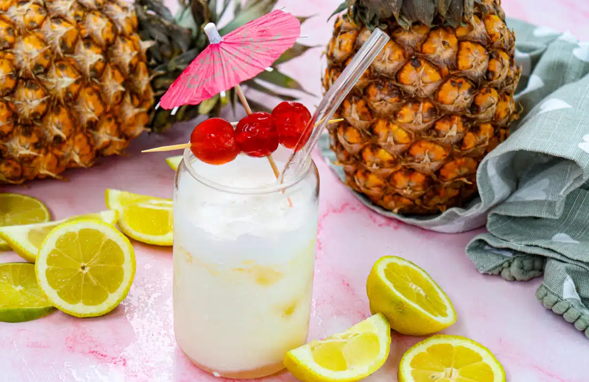 pina colada mocktail in a glass with a straw and fresh pineapples