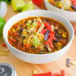 taco soup in bowl with hredded cheese and tortilla strips