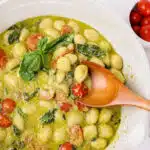 gnocchi pasta with pesto cream sauce and wooden spoon and text overlay