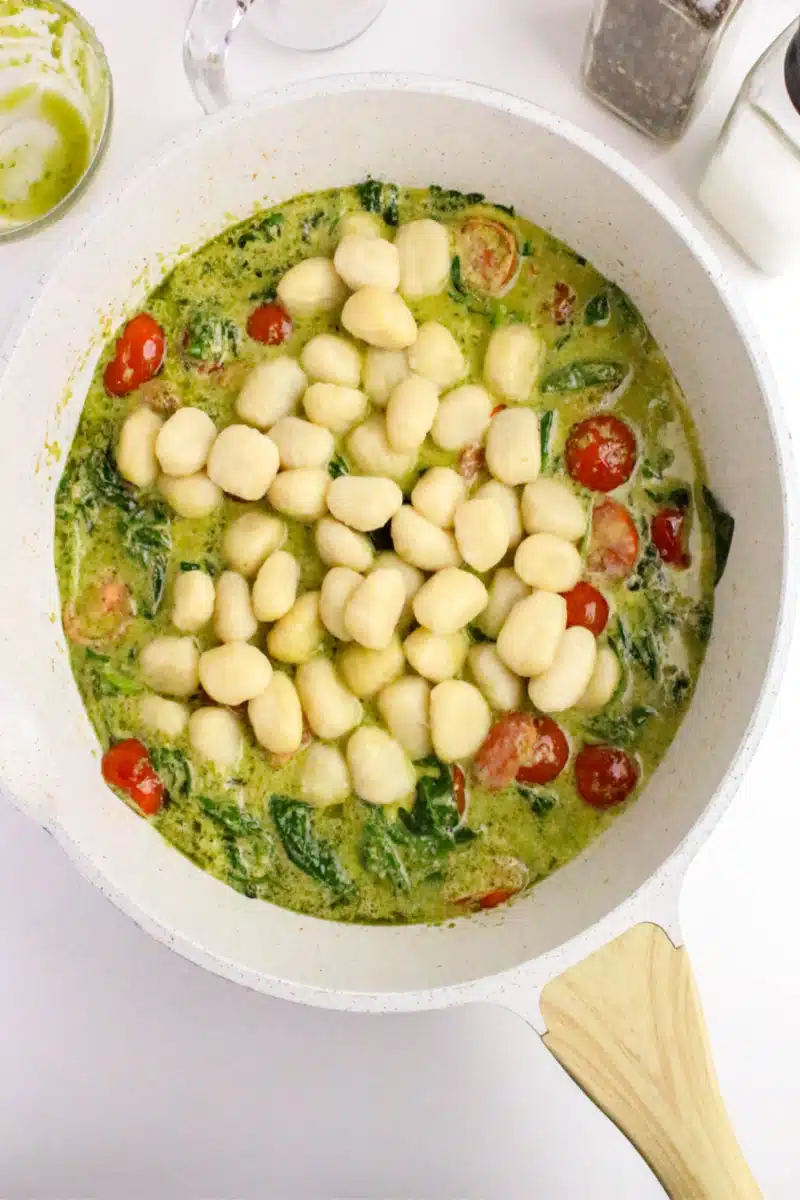 Adding gnocchi to skillet with pesto cream sauce