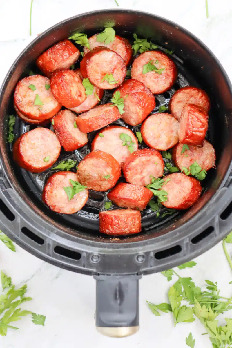 cooked kielbasa in air fryer basket with chopped parsley