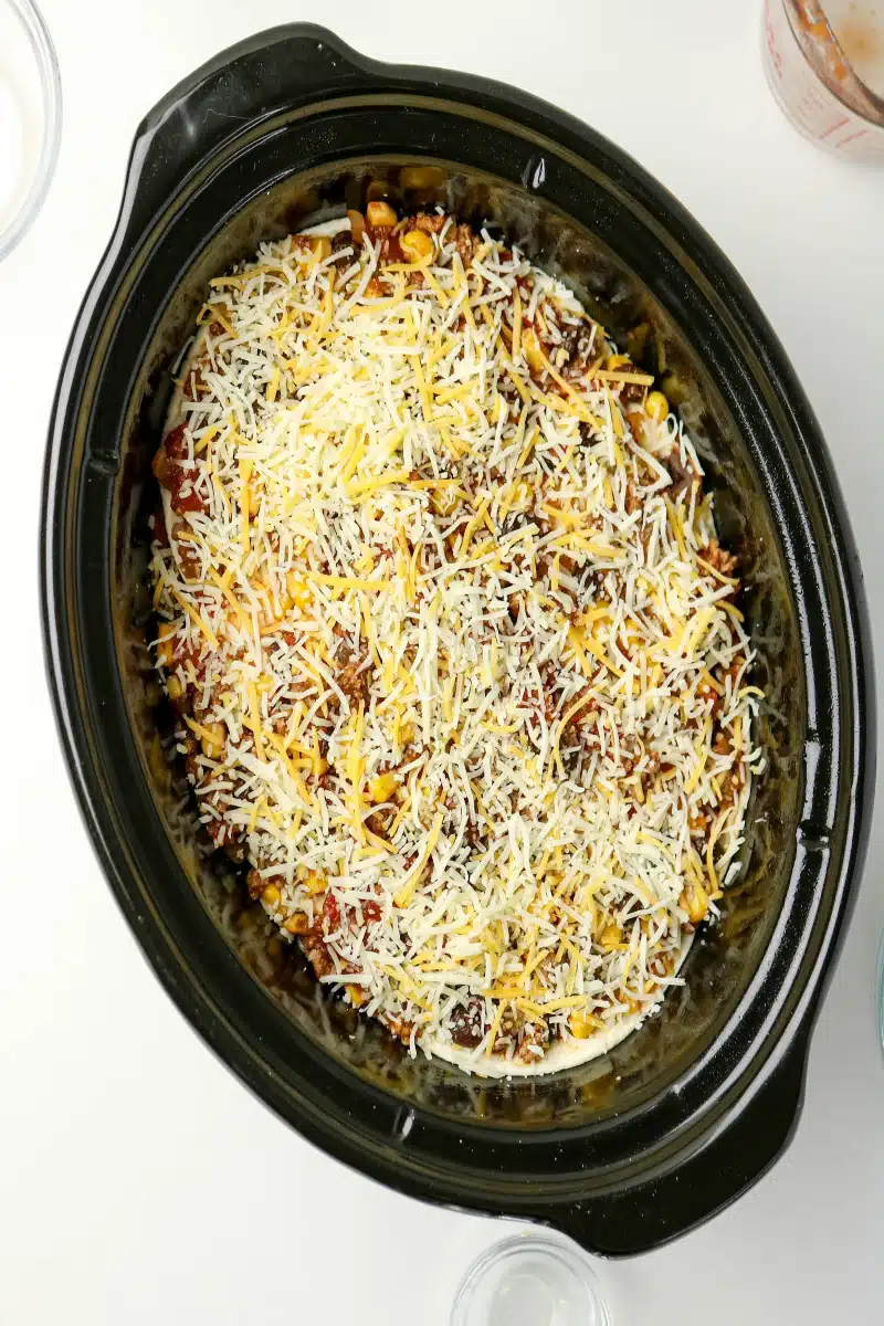 topping the taco casserole with cheese in the slow cooker