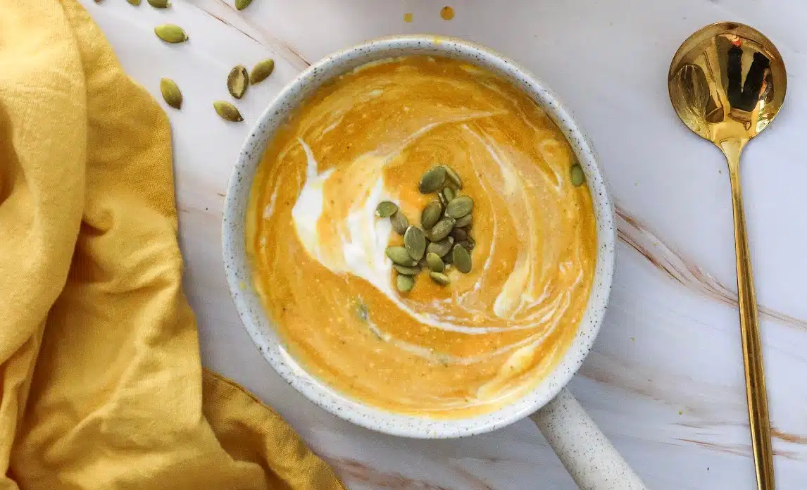 creamy pumpkin soup in a bowl with pumpkin seed granish and a gold spoon