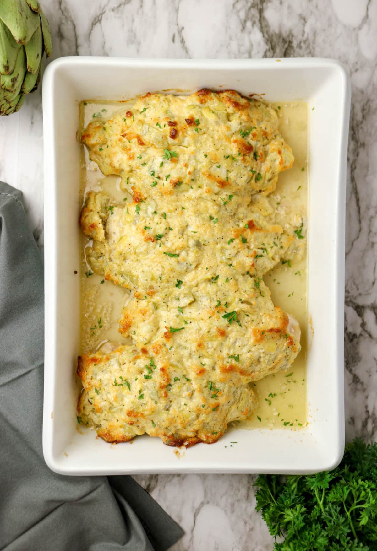overhead of baked chicken in a baking dish with creamy artichoke topping