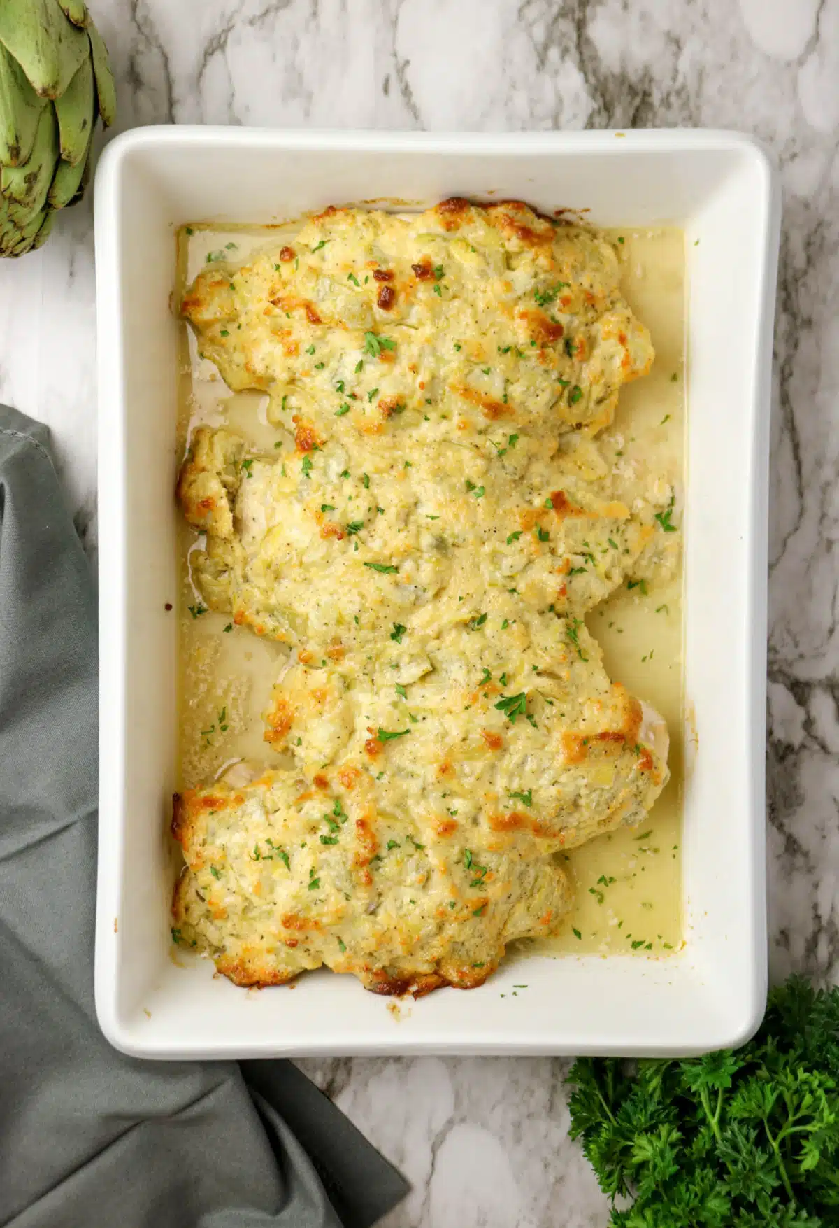 overhead of baked chicken in a baking dish with creamy artichoke topping