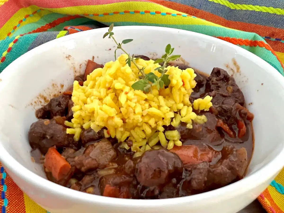 A serving of Caribbean brown chicken stew in a bowl topped with yellow rice