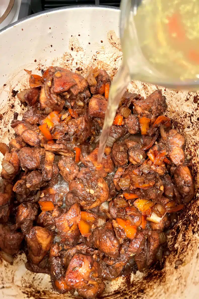 adding broth and tomato paste to the pot