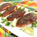 four pieces of blackened chicken on a platter with parsley and lime wedges