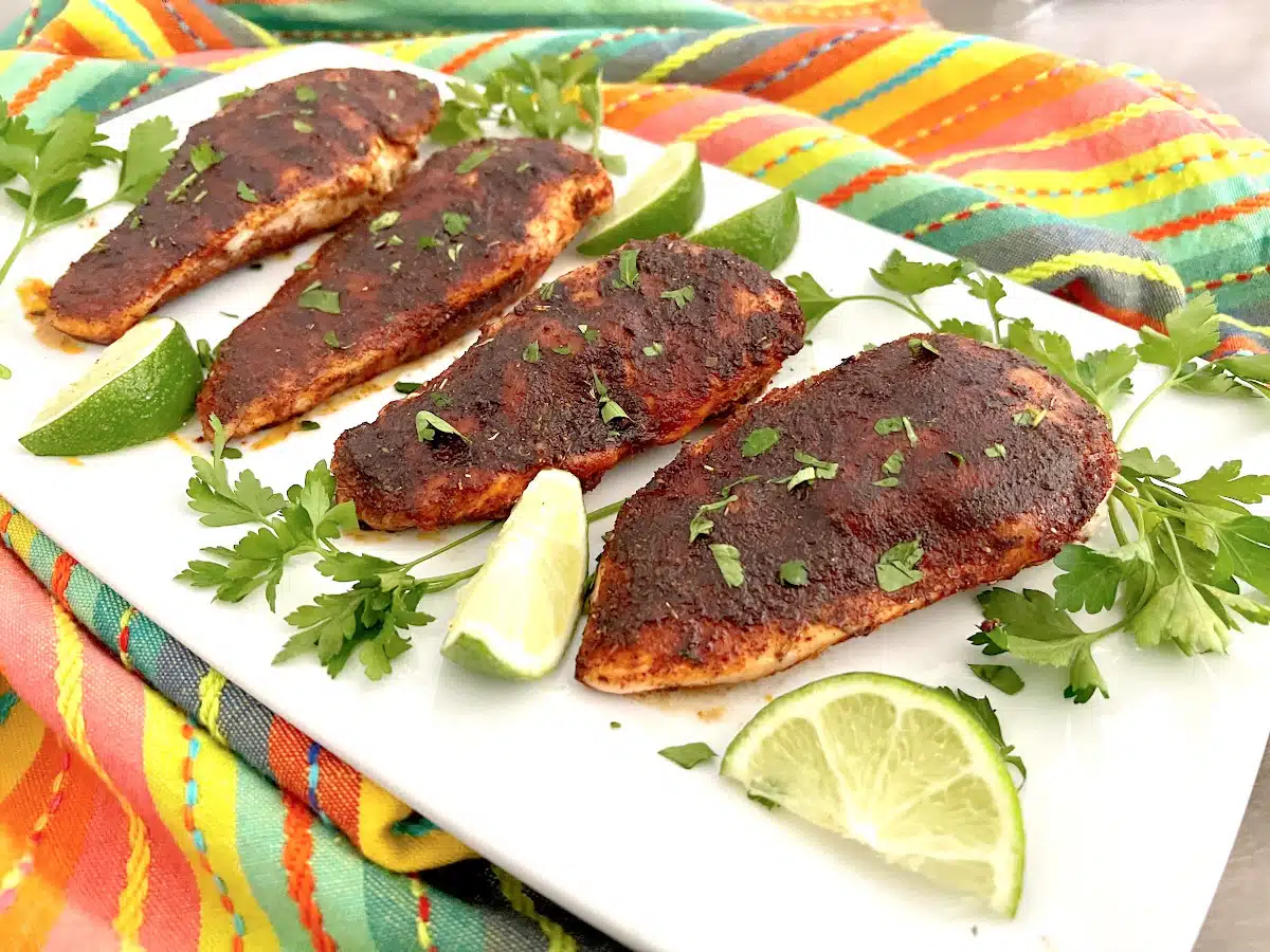 four pieces of blackened chicken on a platter with parsley and lime wedges