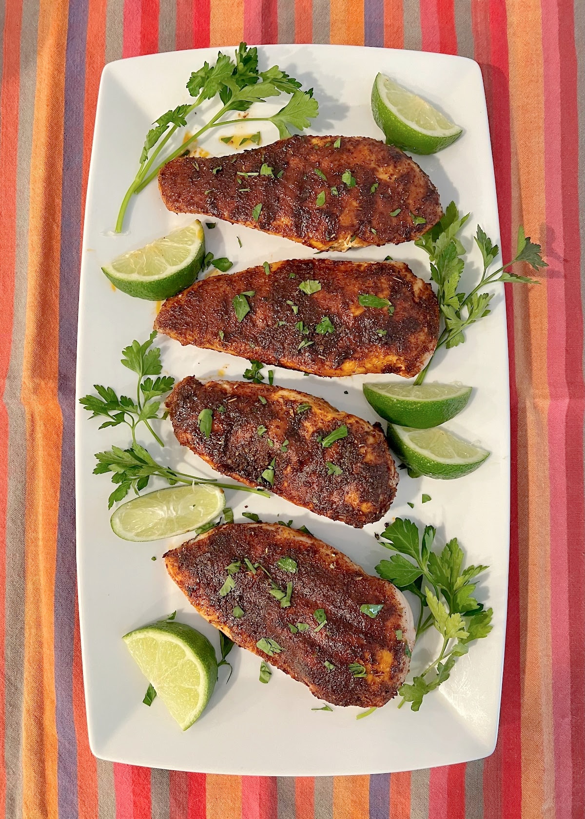 overhead photo of blackened chicken on a platter with a colorful napkin