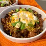 a bowl of beef chili with sour cream, shredded cheese and sliced green onions toppings