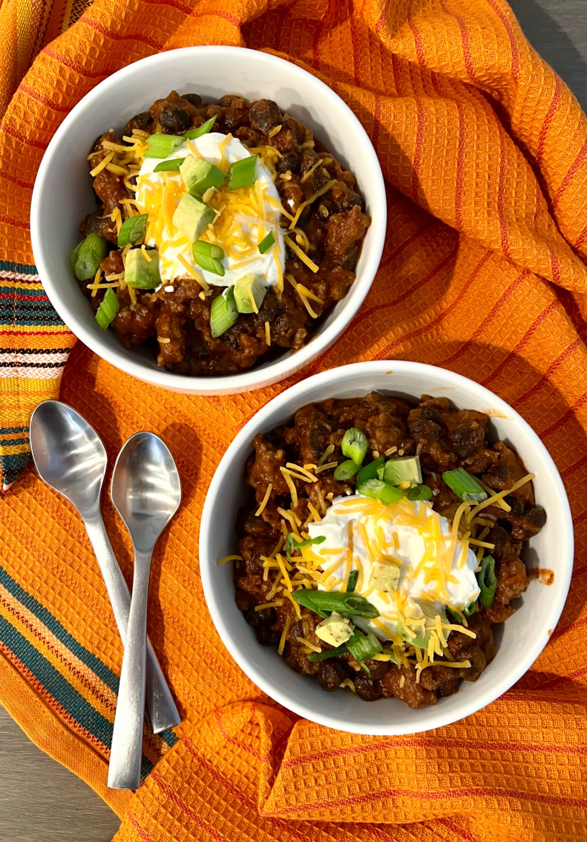 overhead photo of two bowls of easy chili recipe with two spoons on an orange napkin 