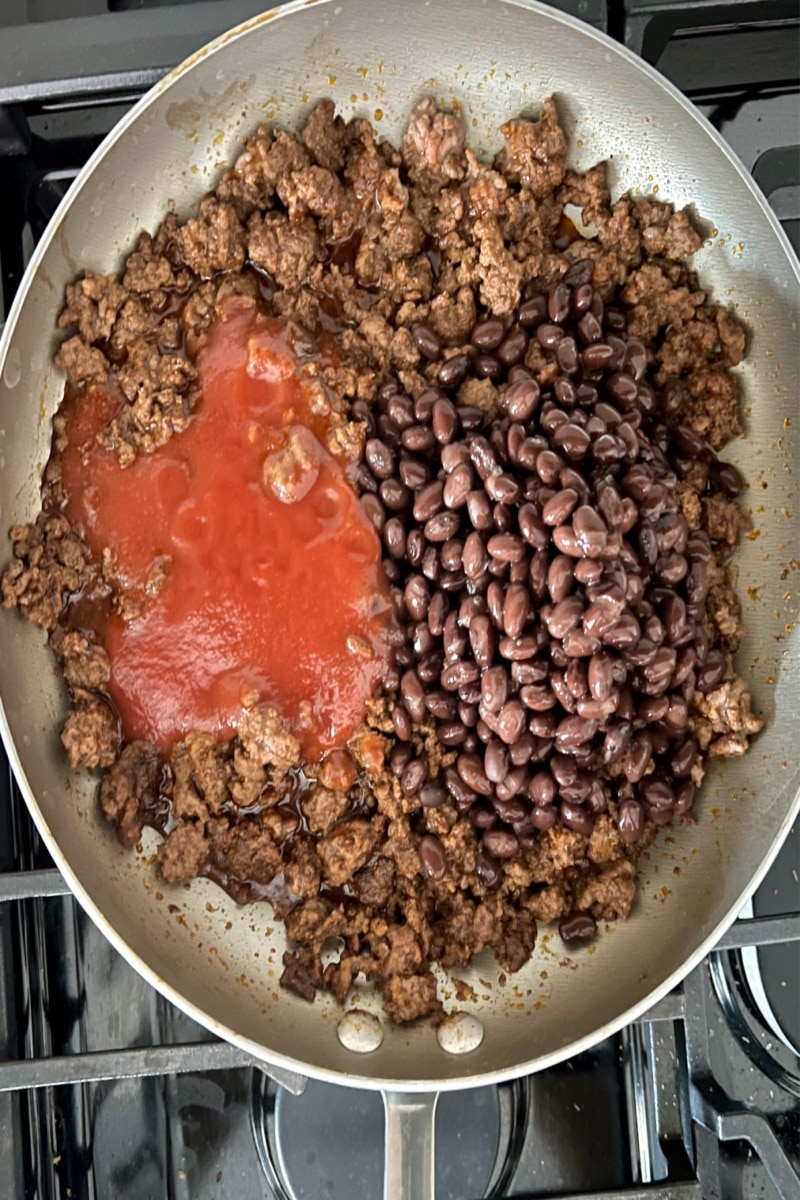 adding black beans and tomato sauce to browned ground beef for chili