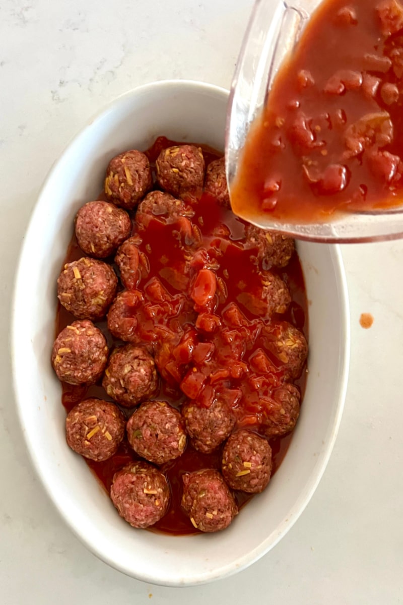pouring taco sauce mixture over mini meatballs in an oval baking dish