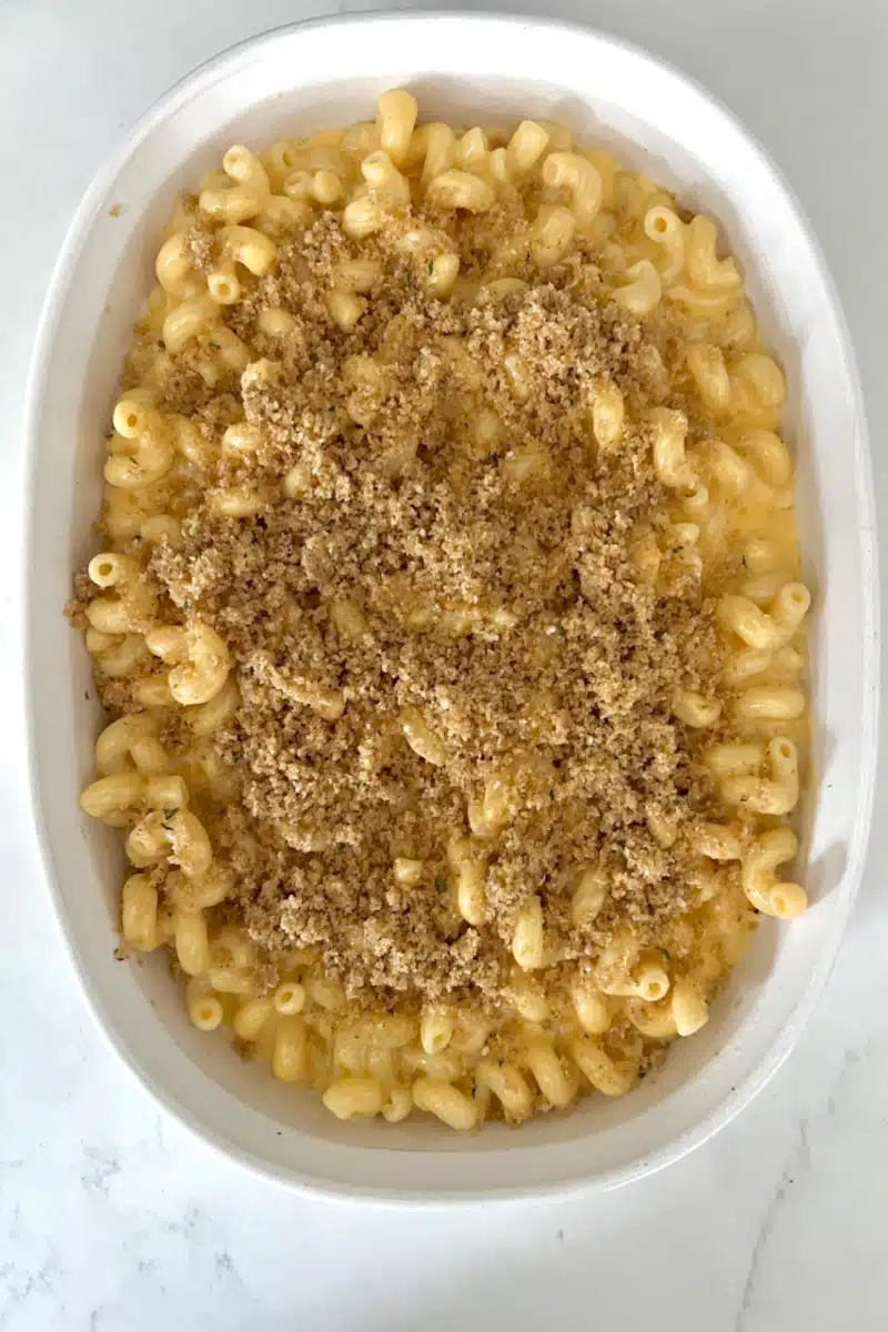 topping mac and cheese in a baking dish with breadcrumb mixture