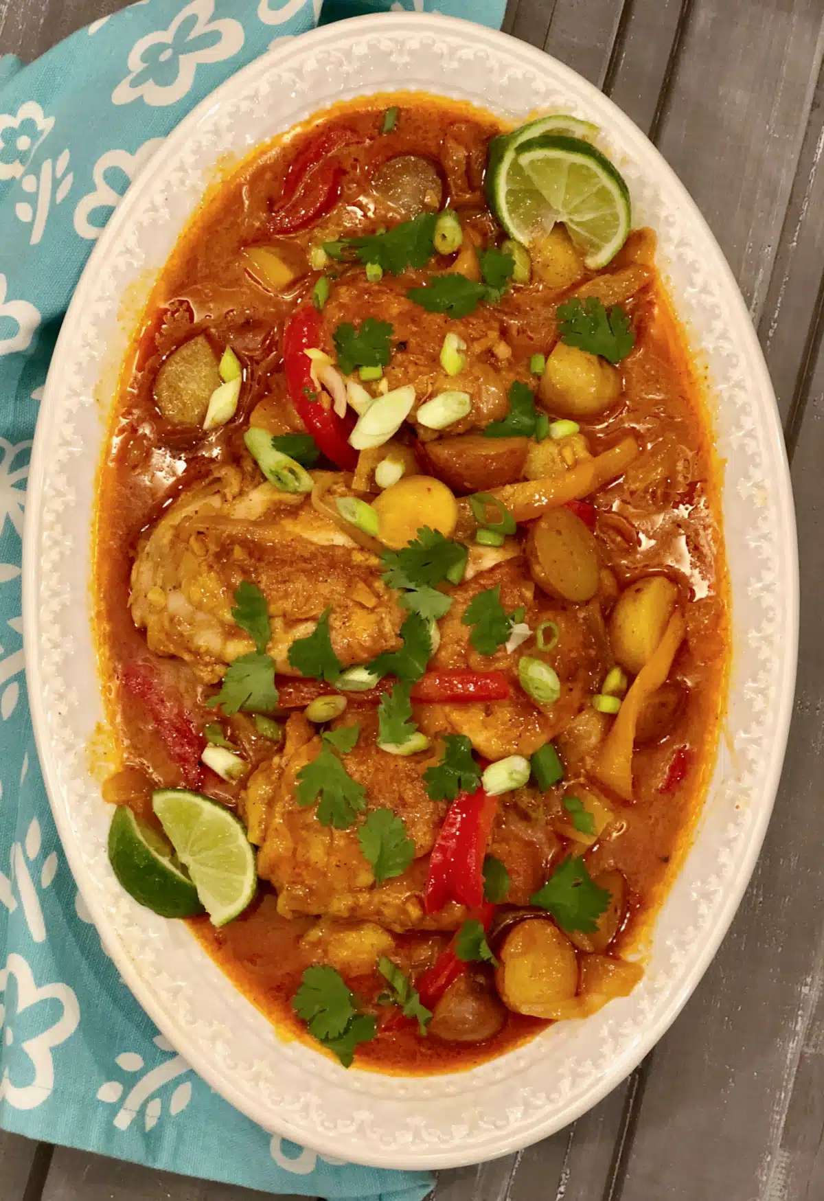 overhead photo of a platter of chicken curry with lime wedges and blue print napkin