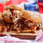 pulled pork sandwiches on a wooden board with a pretty napkin