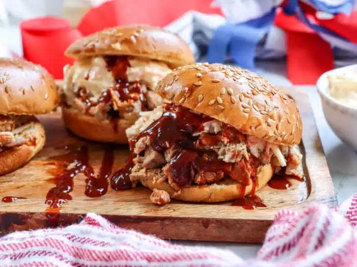 pulled pork sandwiches on a wooden board with a pretty napkin