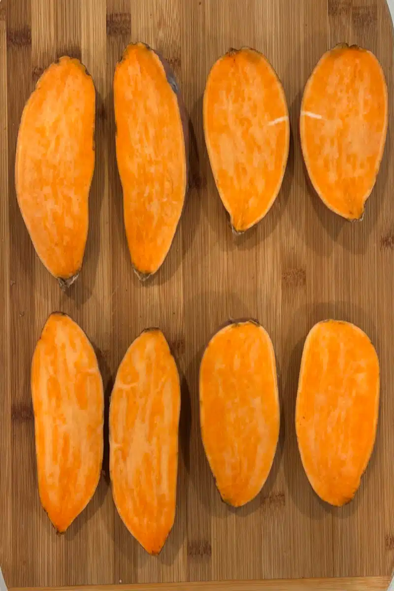 sweet potatoes sliced in half lenghtwise on a wooden cutting board