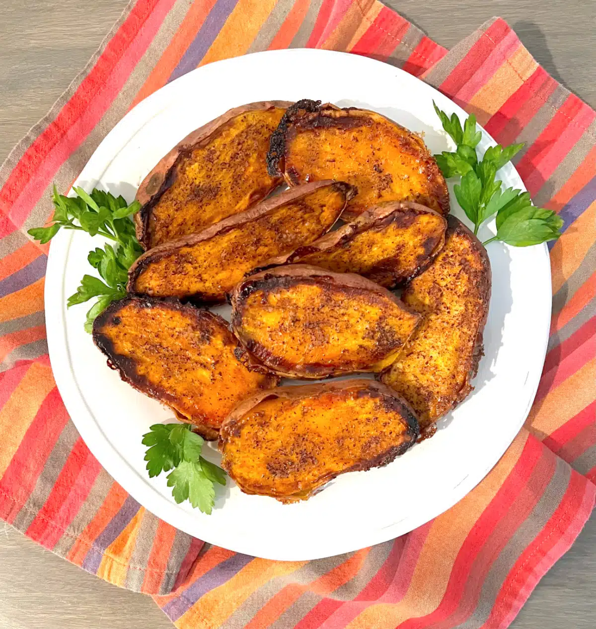 overhead photo of a round platter of candied sweet potato halves with a pretty striped napkin