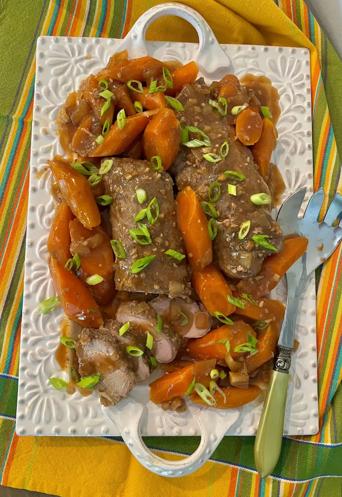 overhead of a platter of honey garlic pork and carrots with a pretty napkin