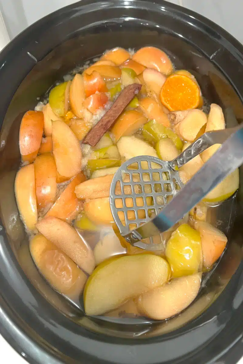 mashing apple cider in the slow cooker with a potato masher