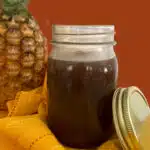 mason jar of homemade sweet nd sour sauce with a pineapple in the background