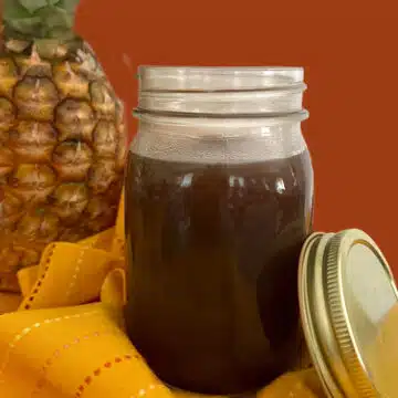 mason jar of homemade sweet nd sour sauce with a pineapple in the background