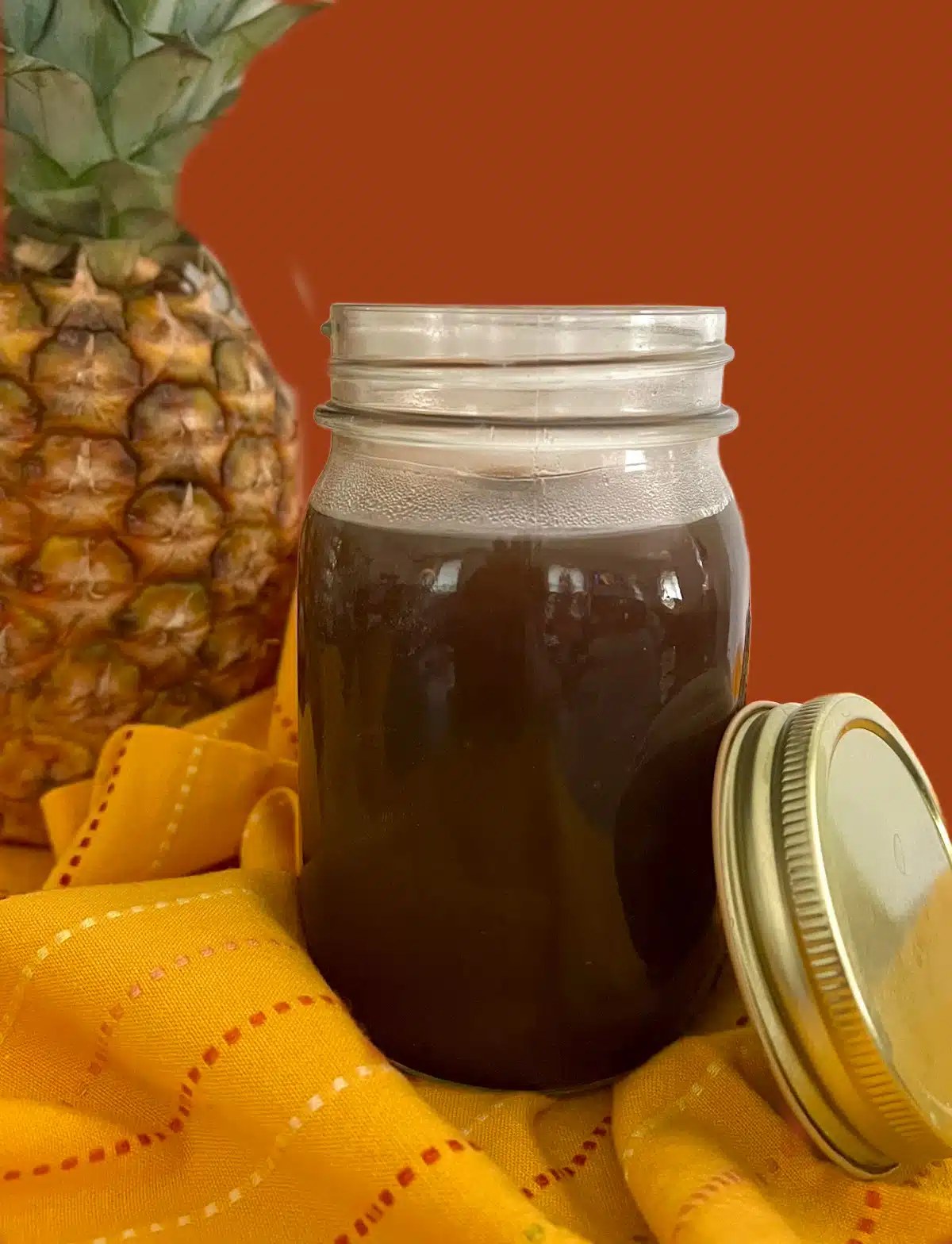 mason jar of homemade sweet nd sour sauce with a pineapple in the background