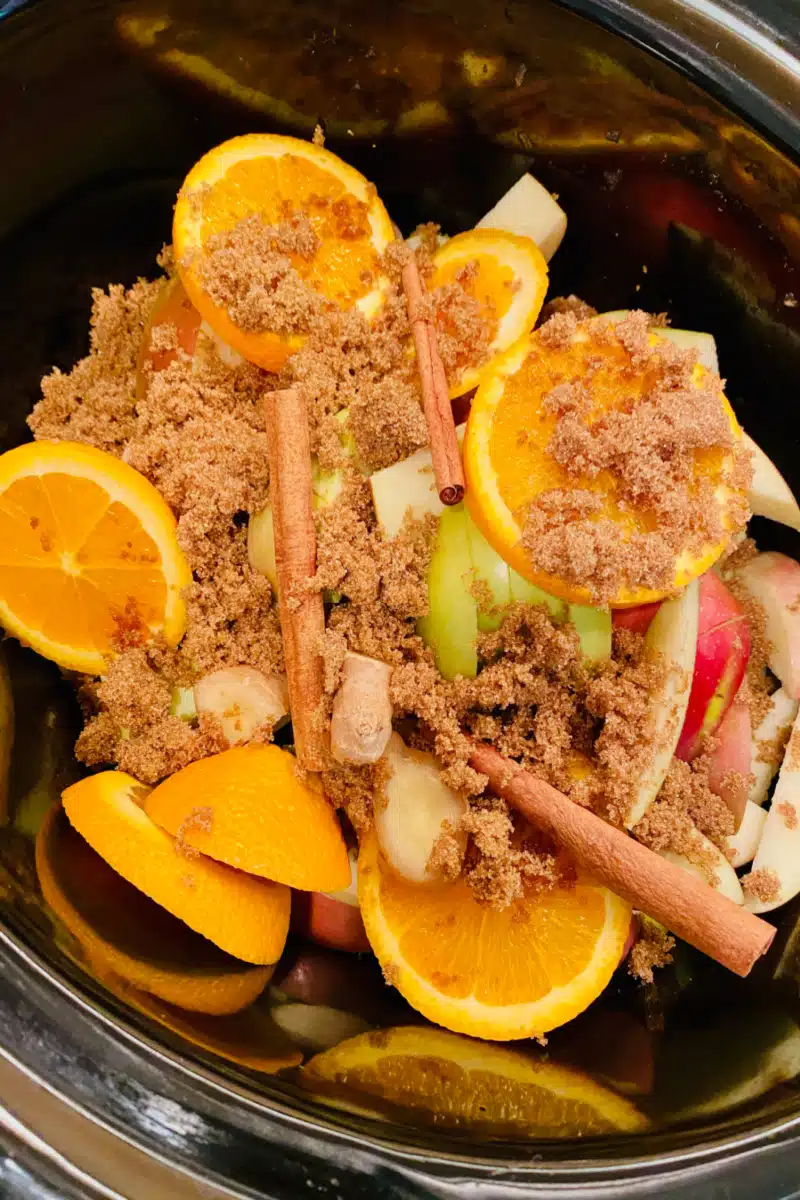 combining apples, oranges and seasonings in slow cooker for apple cider