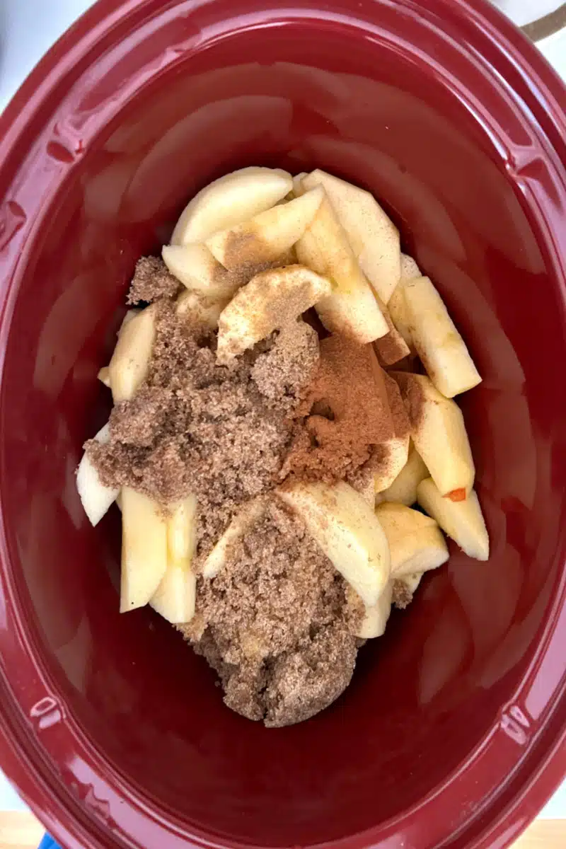 adding brown sugar and spices to sliced apples in a slow cooker