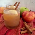 glasses of apple cider with cinnamon sticks and apples