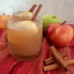 glasses of apple cider with cinnamon sticks and apples