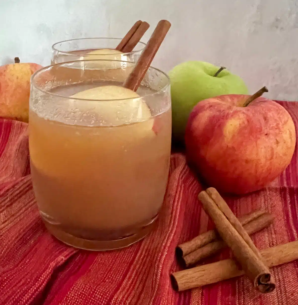 glasses of apple cider with cinnamon sticks and apples