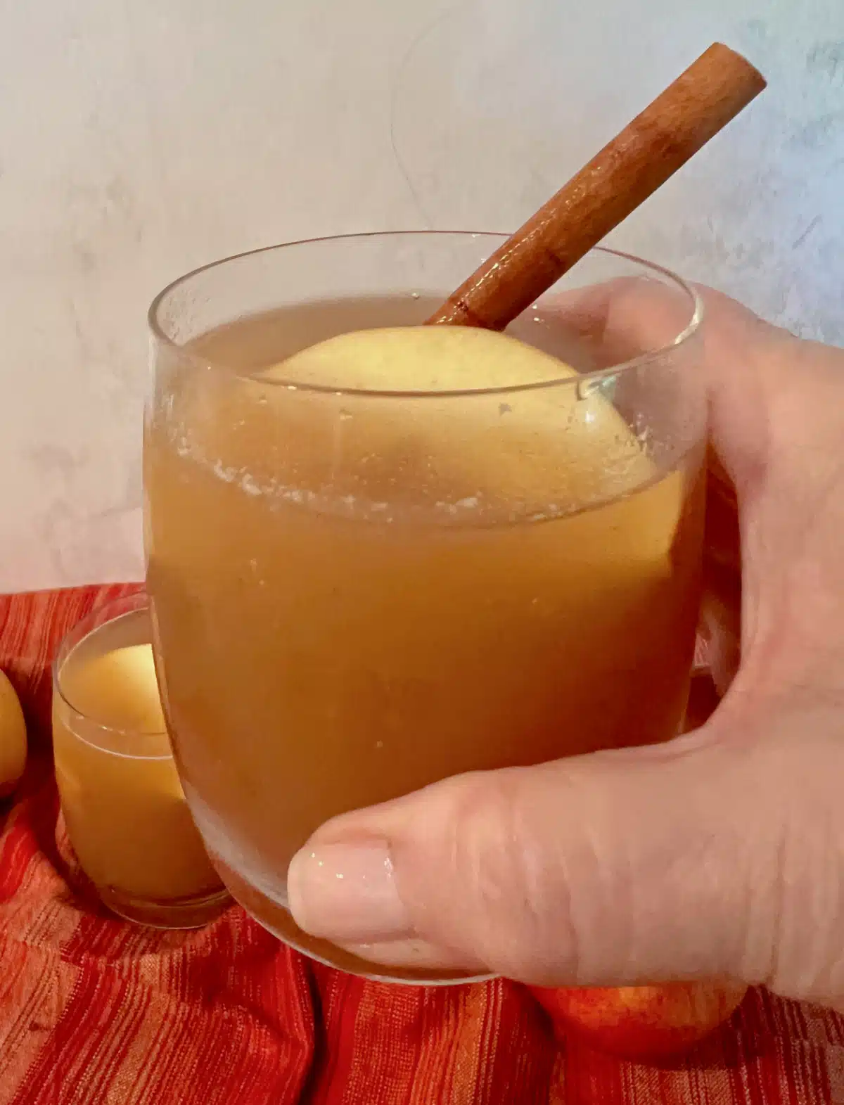 holding a glass of homemade apple cider with a cinnamon stick stirrer